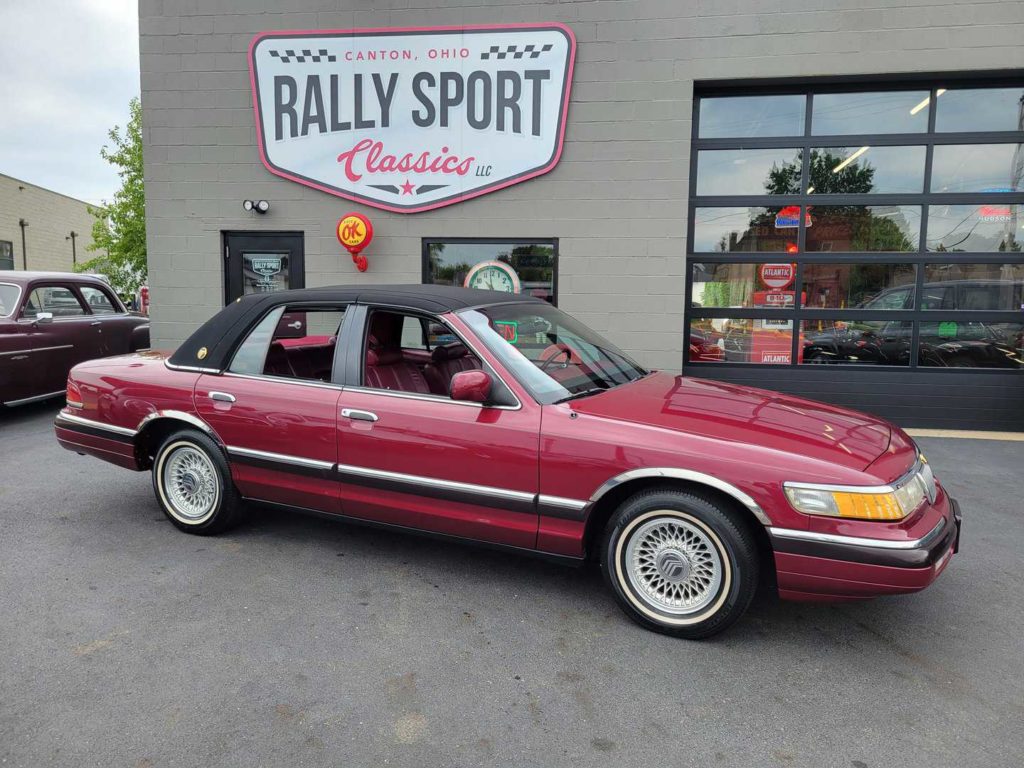 A maroon car is parked in front of a rally sport car dealership.