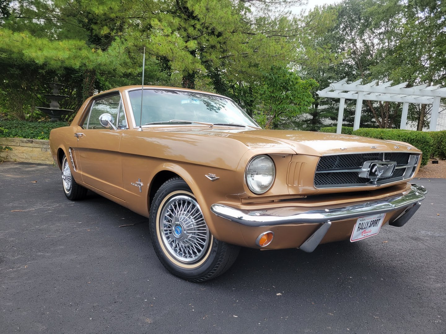 A 1965 tan Ford Mustang parked in a parking lot.