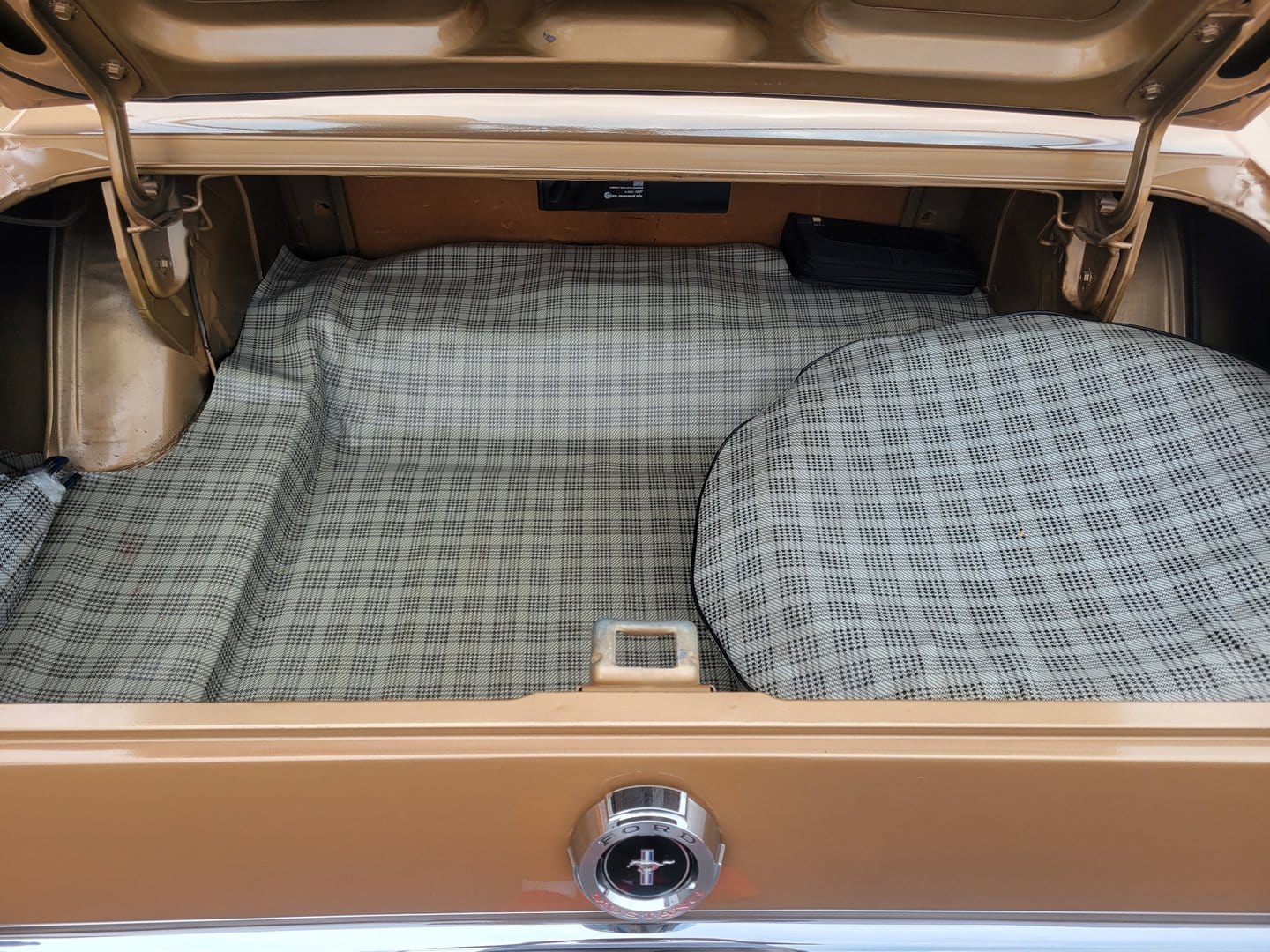 The trunk of a 1965 Ford Mustang with a checkered floor mat.
