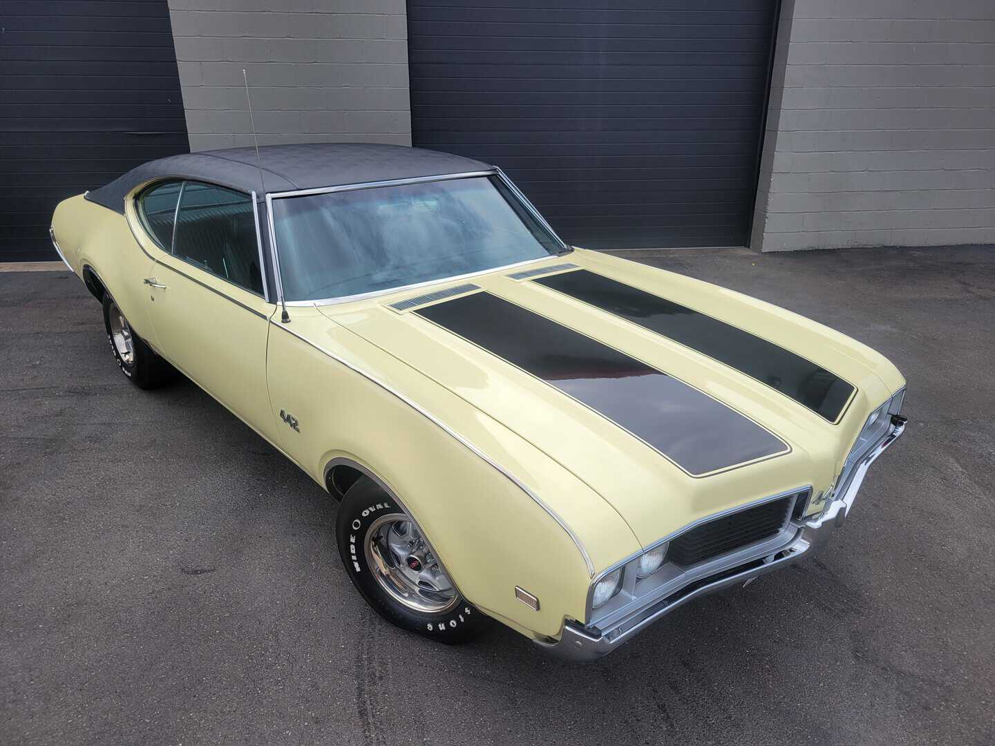 A 1969 Oldsmobile 442 muscle car is parked in front of a garage.