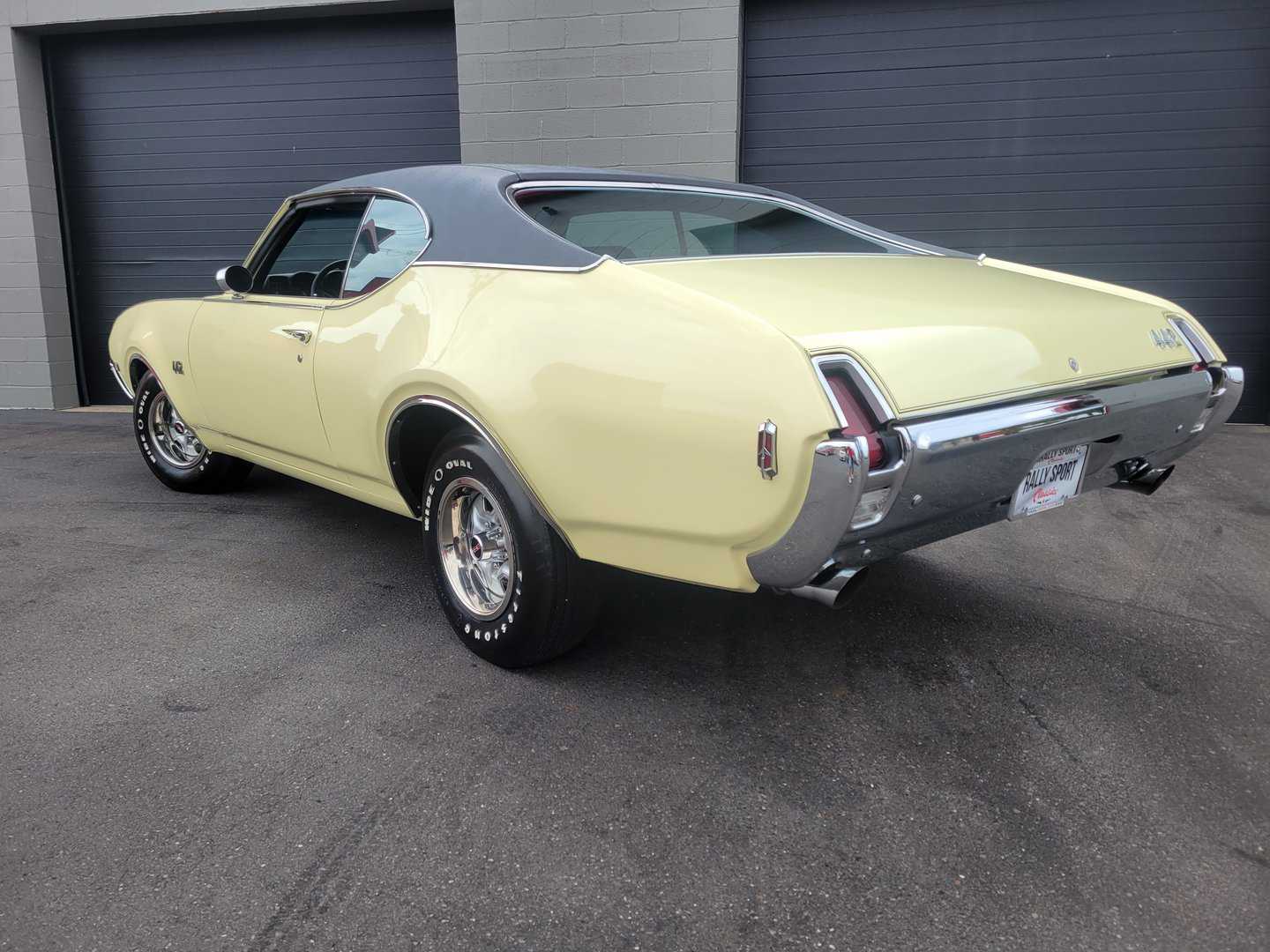 A 1969 yellow Oldsmobile 442 muscle car parked in front of a garage.