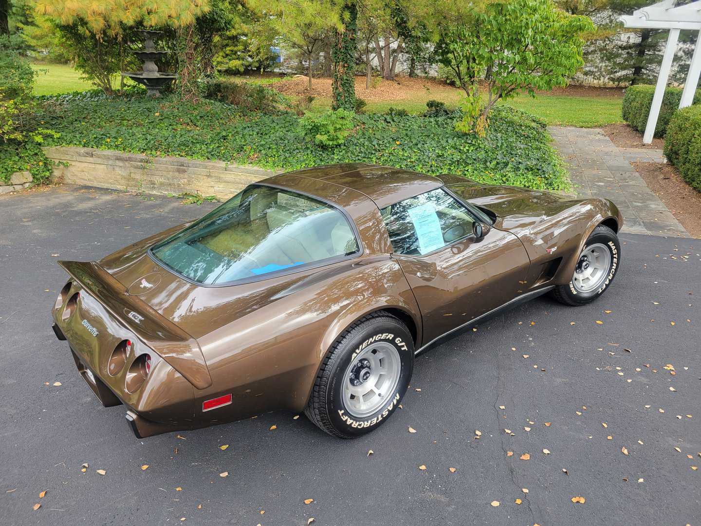 A brown 1979 Chevrolet Corvette parked in front of a house.