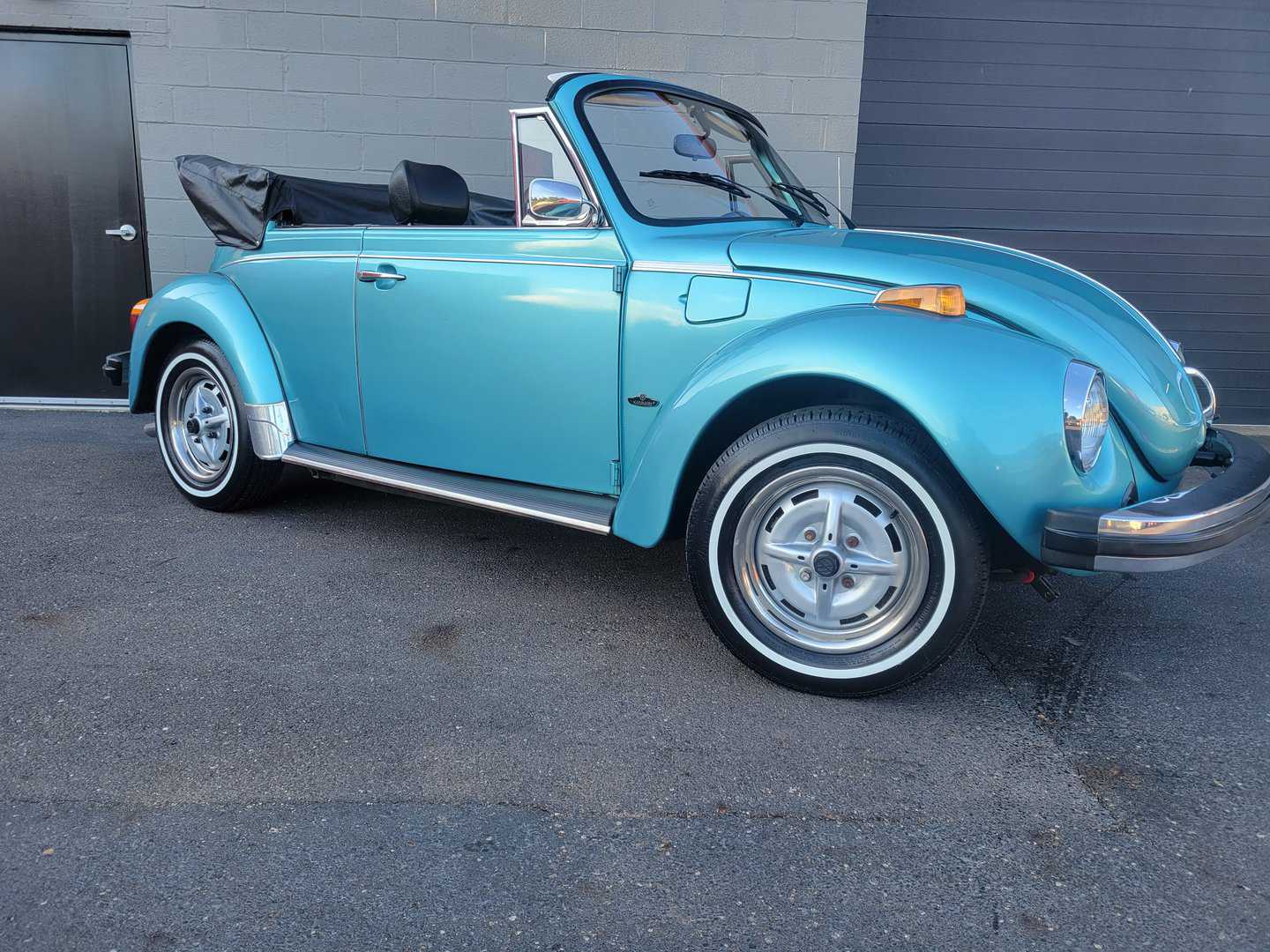 A 1979 blue Volkswagen Beetle Convertible parked in front of a building.