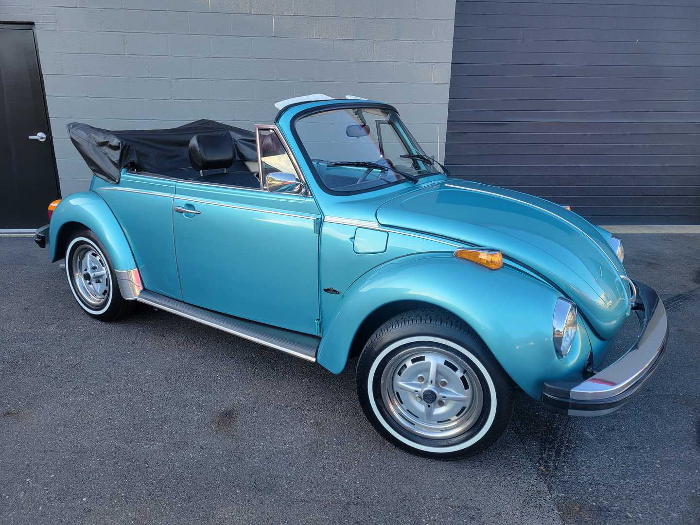 A 1979 blue Volkswagen Beetle Convertible parked in front of a building.