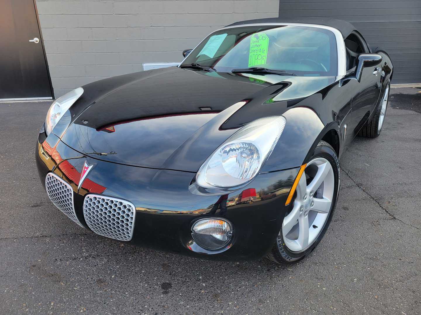 A 2006 Black Pontiac Solstice Is Parked In Front Of A Building.