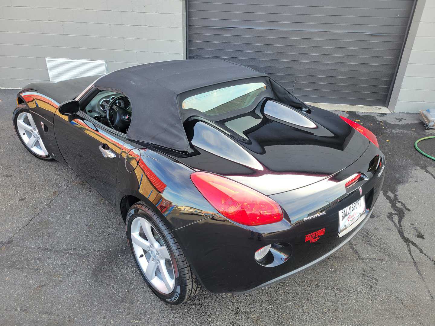 A 2006 Pontiac Solstice, A Sleek Black Sports Car, Parked In Front Of A Garage.