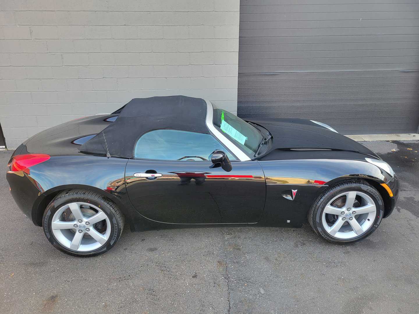 A 2006 Black Pontiac Solstice Sports Car Parked In Front Of A Garage.