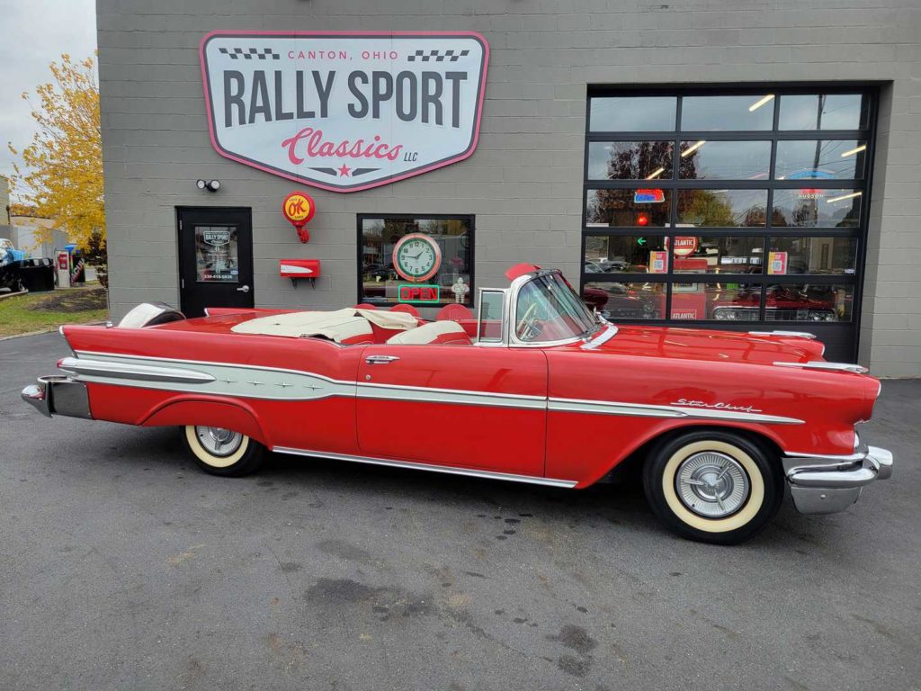 A Red Pontiac Starchief Convertible, Parked In Front Of A Rally Sport Classic Car Shop.