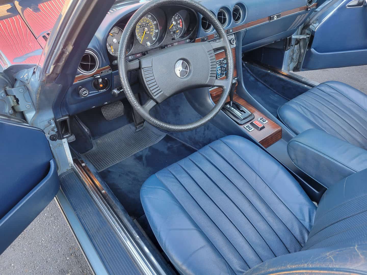 The Interior Of A 1979 Mercedes Benz 450 Sl, Featuring Blue Leather Seats And A Matching Steering Wheel.