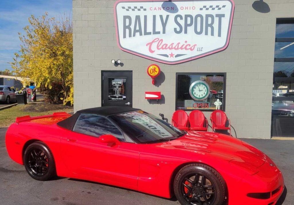 A Red Convertible Corvette Parked In Front Of A Rally Sport.